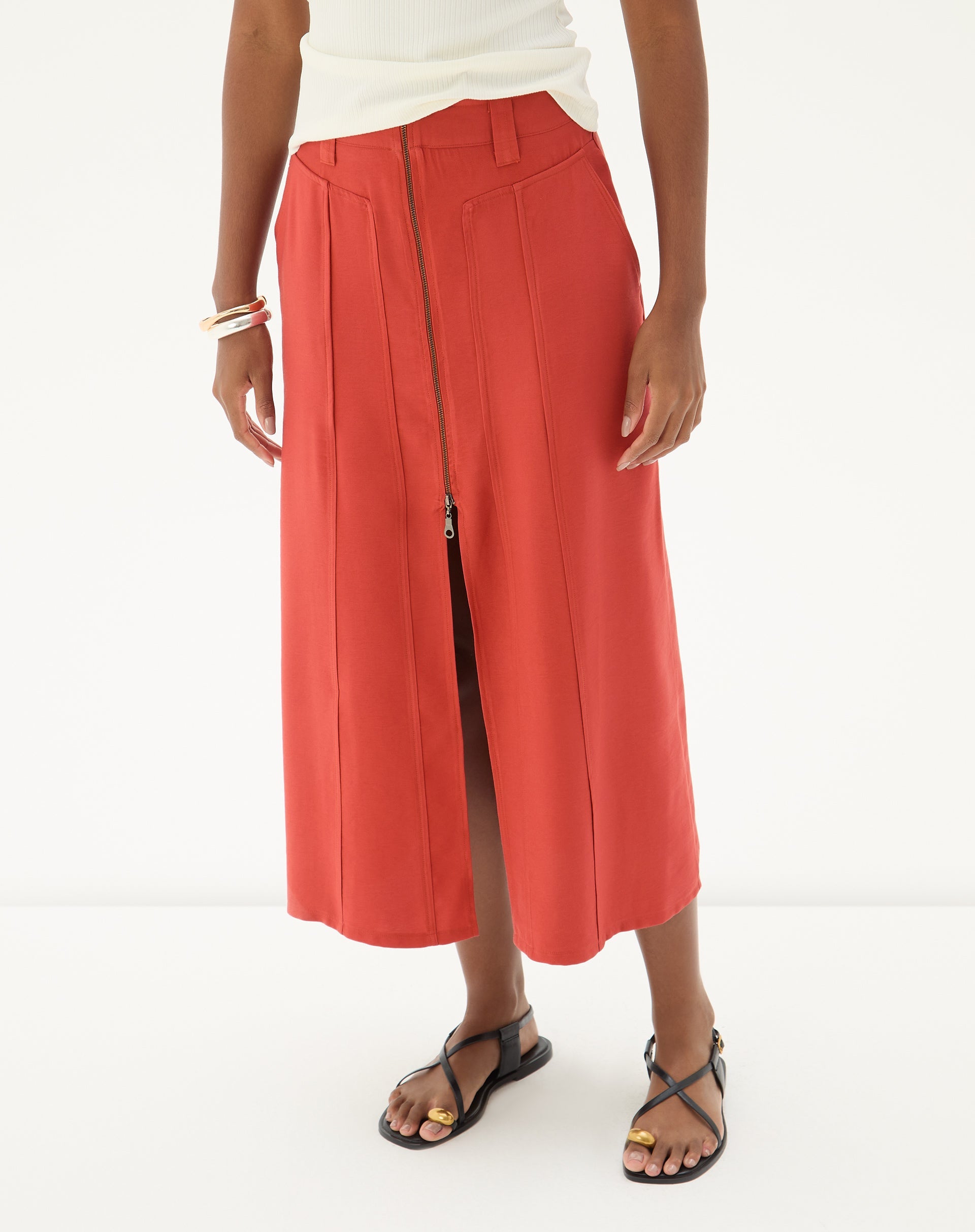 Vista lateral da saia midi marrom com fenda, modelo usando sandálias.