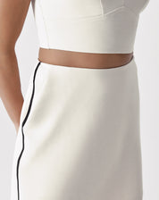 Modelo vestindo saia curta slim de alfaiataria bege com botas pretas, vista traseira.