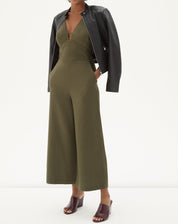 Imagem de um macacão verde com alças largas e decote em V, combinado com uma jaqueta preta.