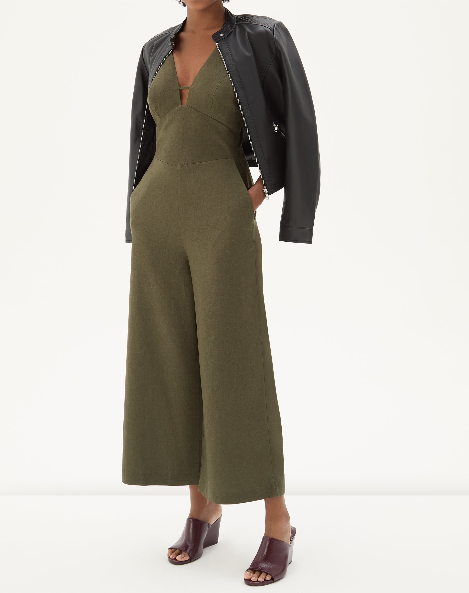 Imagem de um macacão verde com alças largas e decote em V, combinado com uma jaqueta preta.