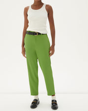 Modelo vestindo calça verde cropped com camisa branca sem mangas e sapatos pretos.