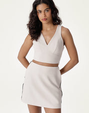 Vista frontal completa da blusa decote V alfaiataria bege, combinada com saia.