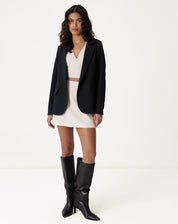 Look completo com blusa decote V alfaiataria bege, saia e blazer preto, ideal para ocasiões formais.