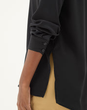 Vista lateral da camisa preta de manga longa, destacando a barra reta e o ajuste regular.