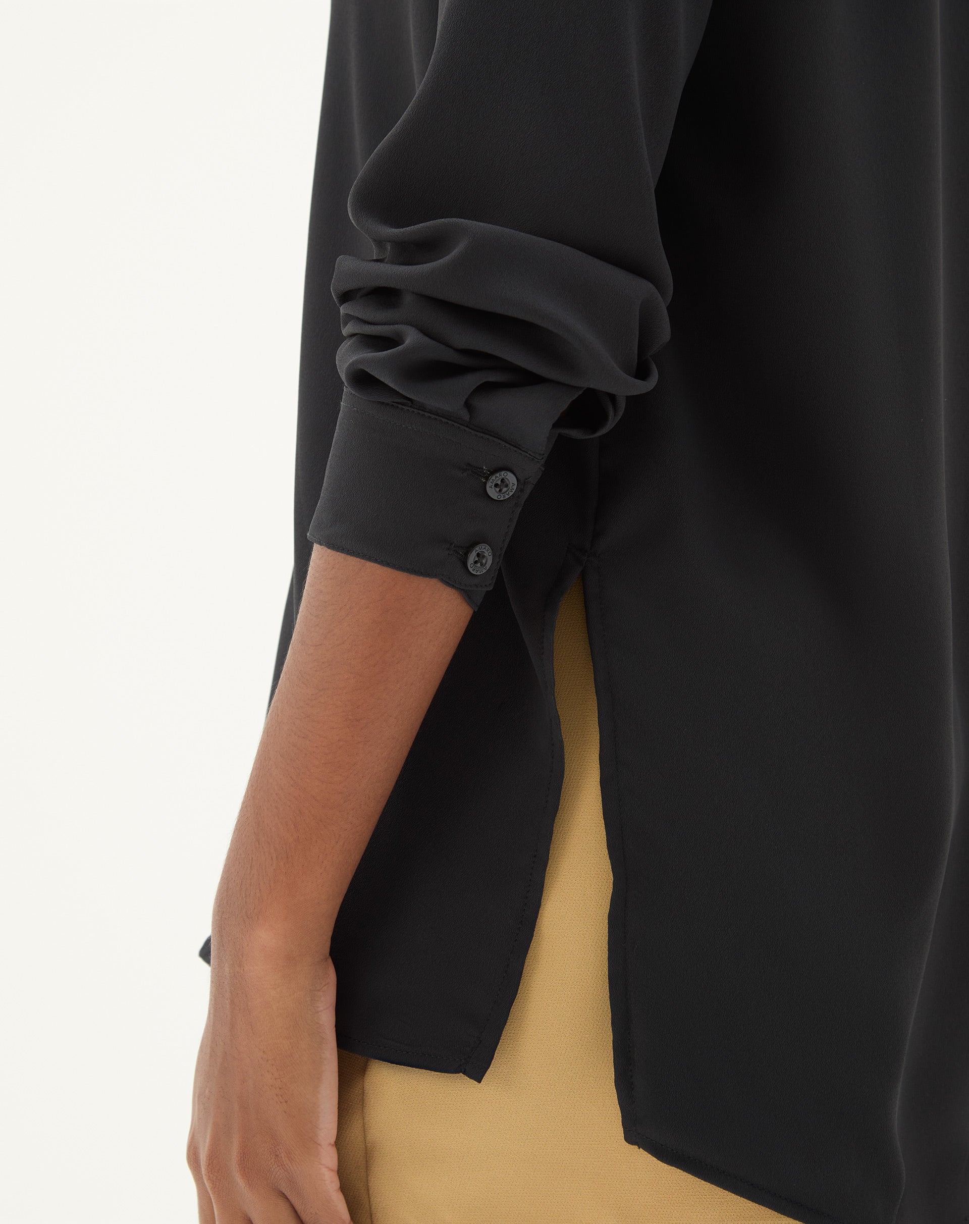 Vista lateral da camisa preta de manga longa, destacando a barra reta e o ajuste regular.