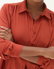 Detalhe do punho simples e fechamento com botões da camisa marrom.