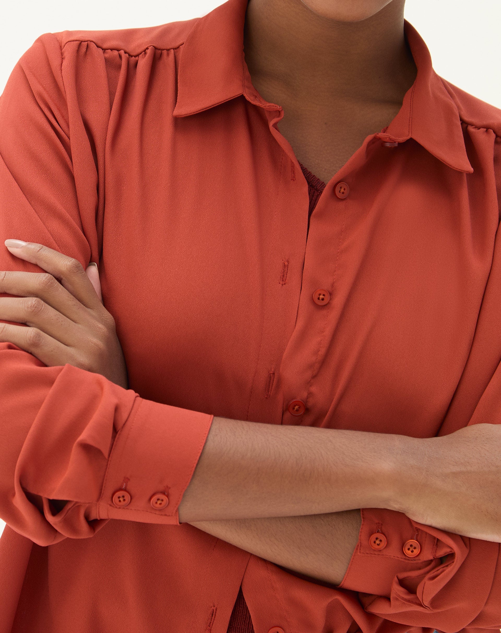 Detalhe do punho simples e fechamento com botões da camisa marrom.