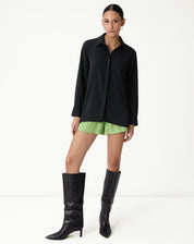 Vista completa da camisa preta de manga longa com barra reta, combinada com shorts verdes.