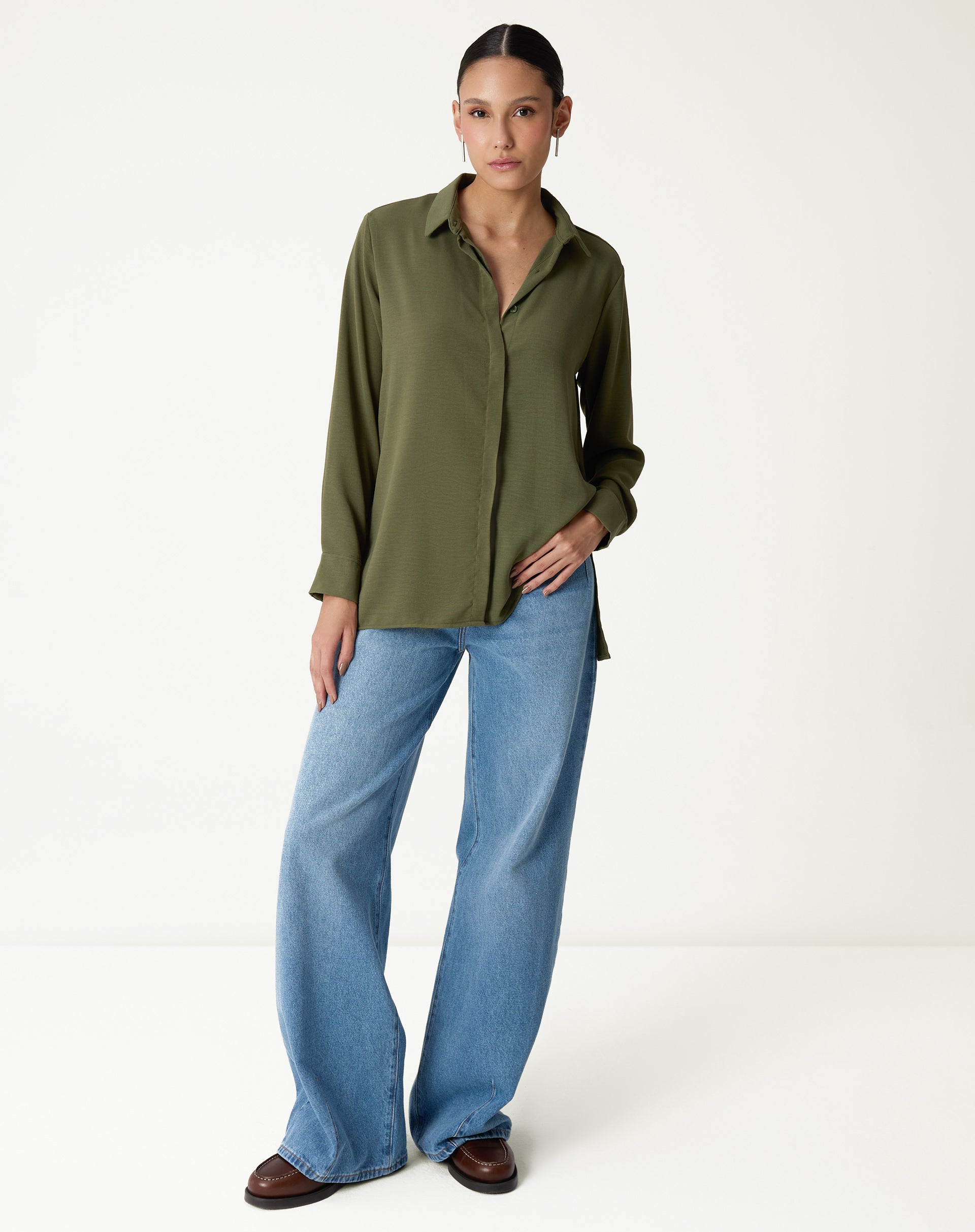 Modelo vestindo camisa verde de manga longa com barra reta e calça jeans.