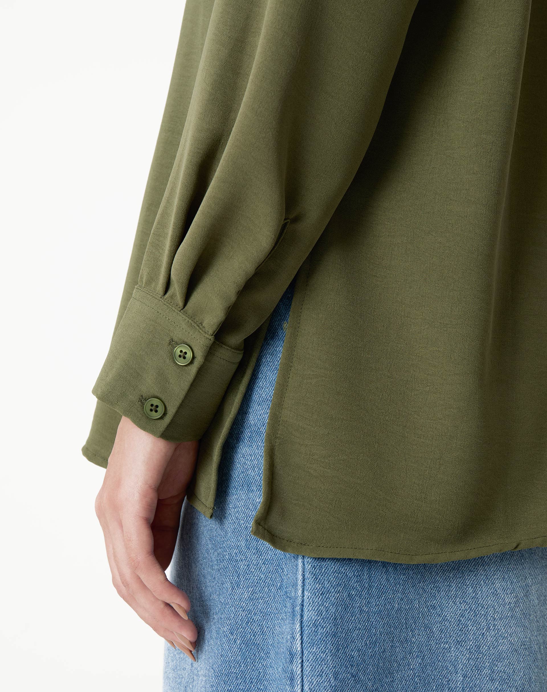 Detalhe do punho simples com botão da camisa verde.