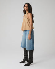 Modelo vestindo blusa frente única areia com bermuda jeans e botas pretas.