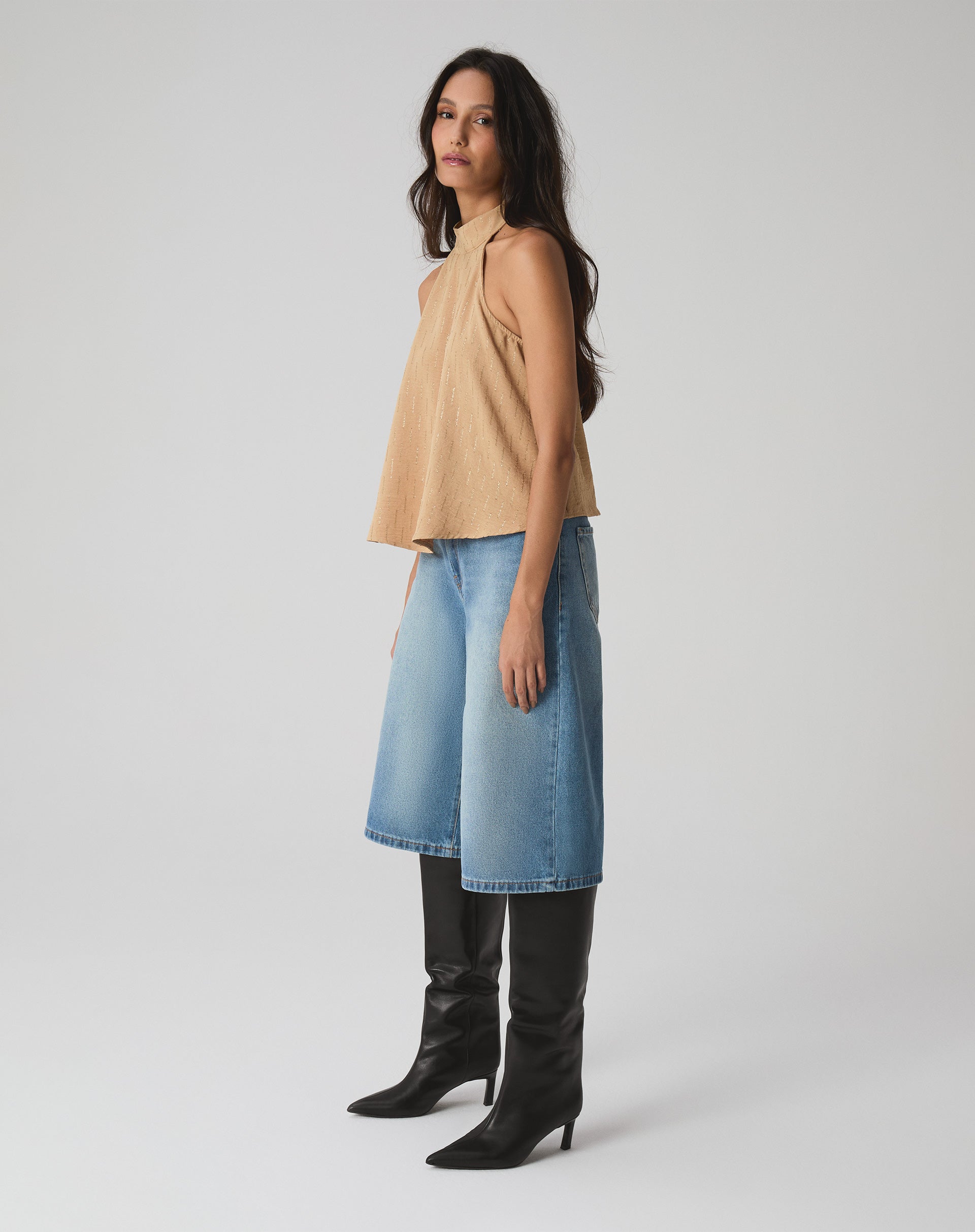 Modelo vestindo blusa frente única areia com bermuda jeans e botas pretas.