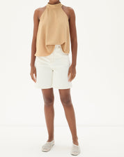 Modelo vestindo blusa frente única areia com bermuda branca e sapatos casuais.