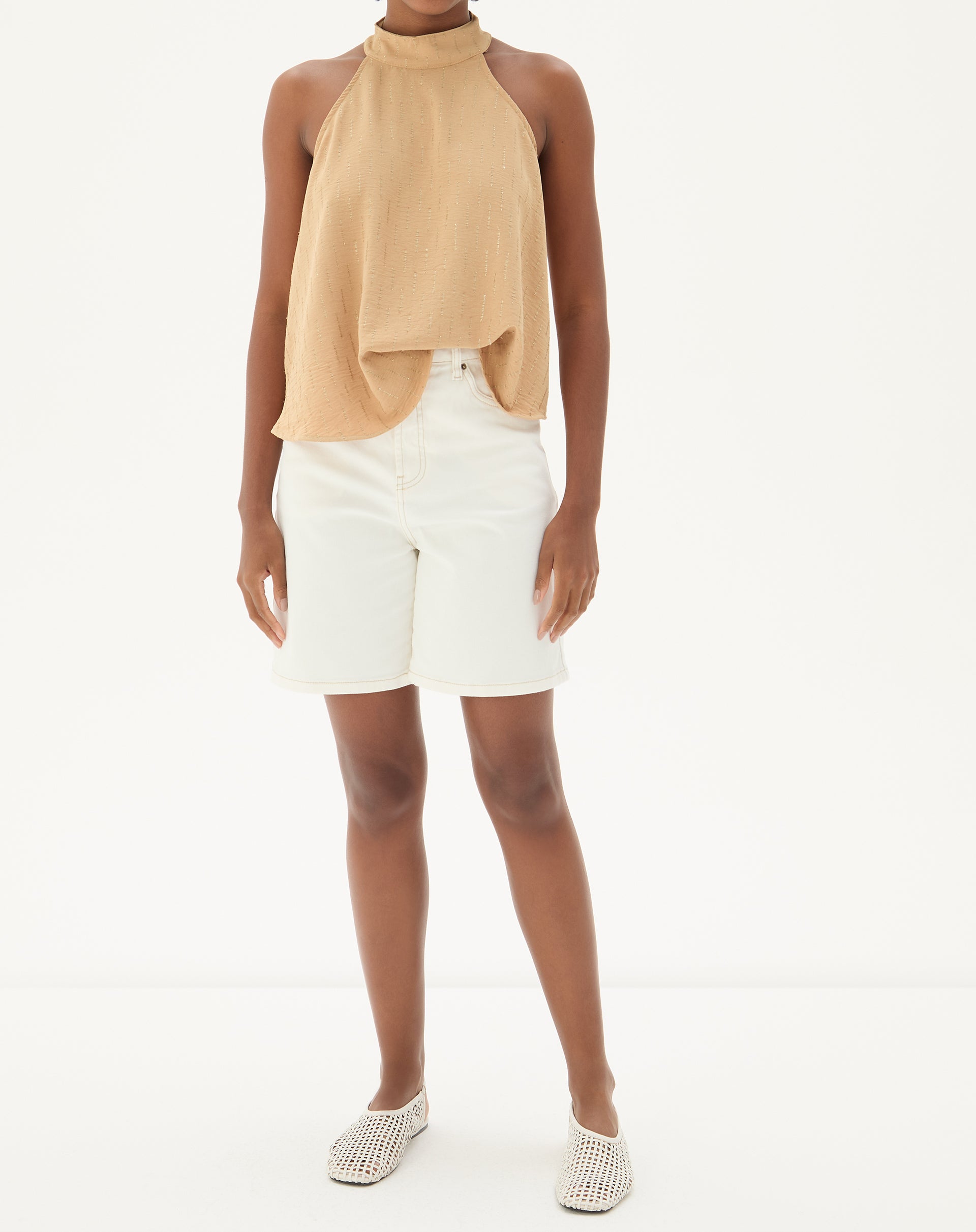 Modelo vestindo blusa frente única areia com bermuda branca e sapatos casuais.