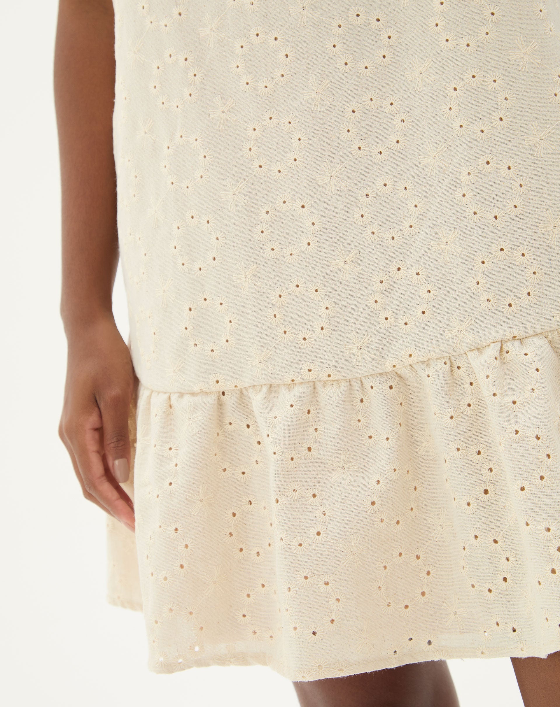 Detalhe do bordado floral no tecido bege do vestido curto.