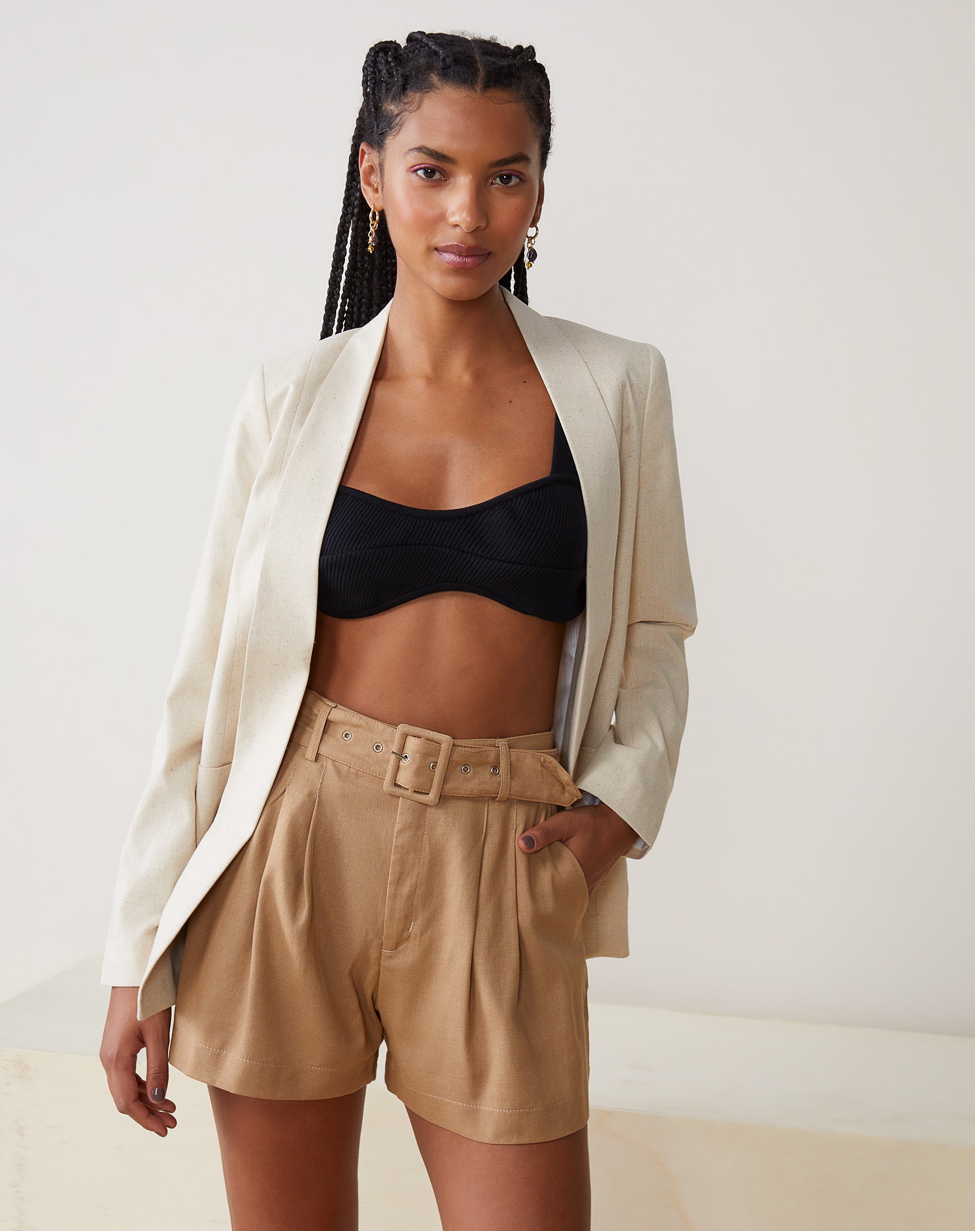 Top curto de tricô preto combinado com blazer branco e shorts bege.