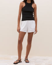 Modelo vestindo blusa preta de tricô com decote halter, combinada com shorts brancos.