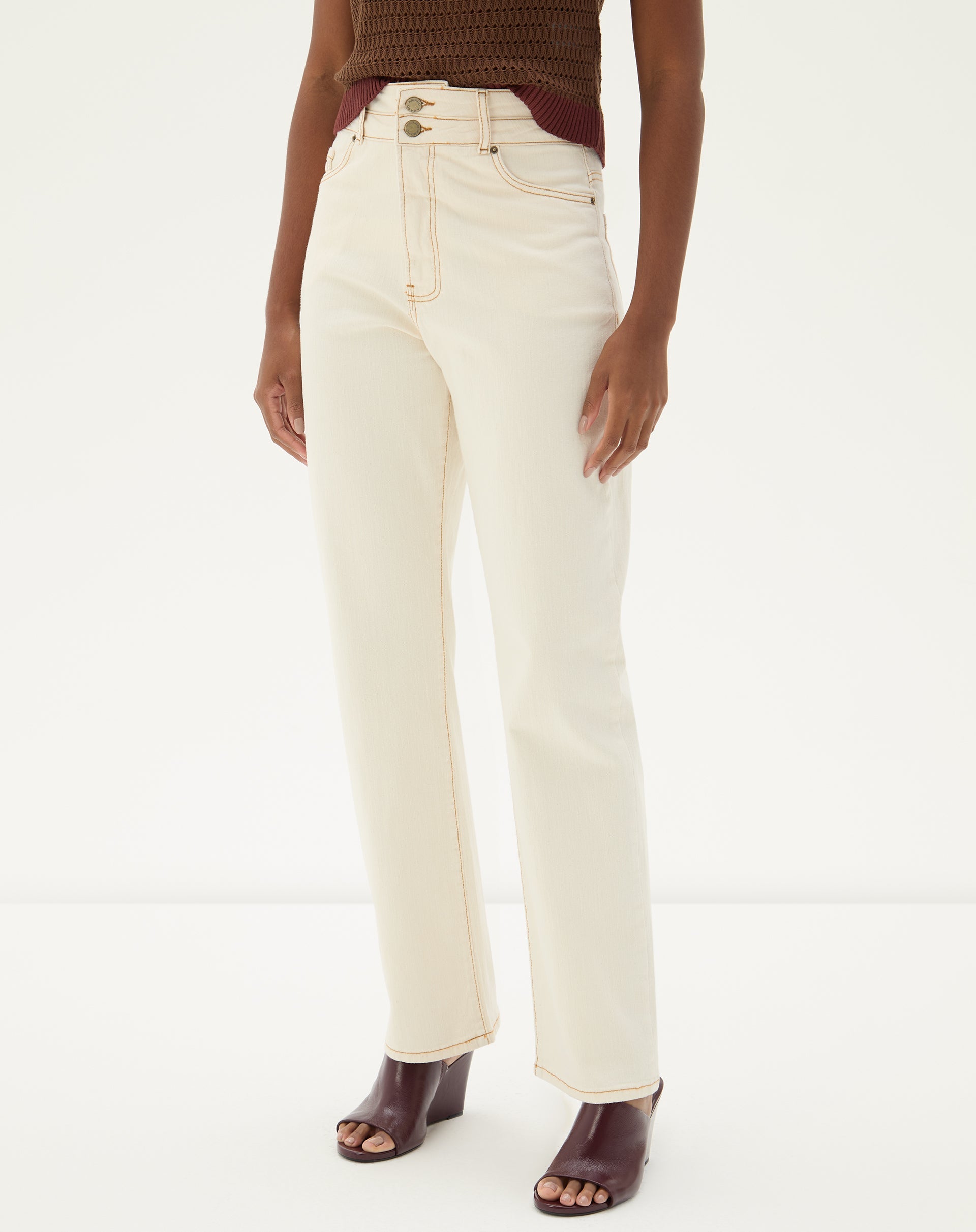 Detalhe da cintura alta e fechamento por botão da calça reta em sarja bege.