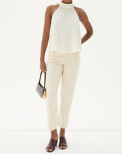 Modelo vestindo calça bege com blusa sem mangas e sandálias, segurando uma bolsa.