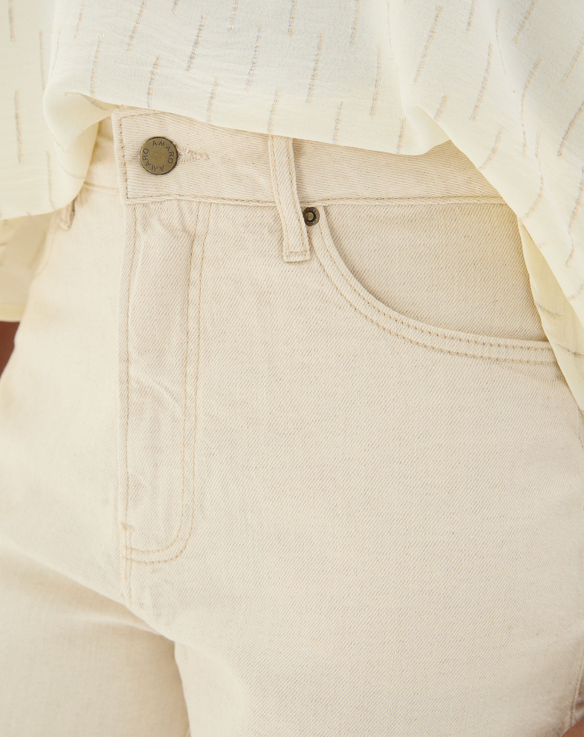 Detalhe do cós e fechamento da calça bege em tecido de sarja.
