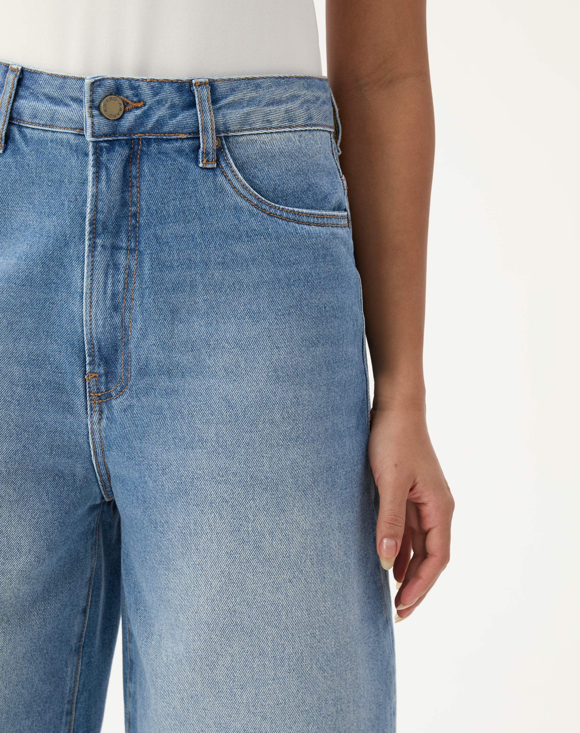 Close-up da frente da bermuda jeans alongada evasê mostrando detalhes do cós e botão.