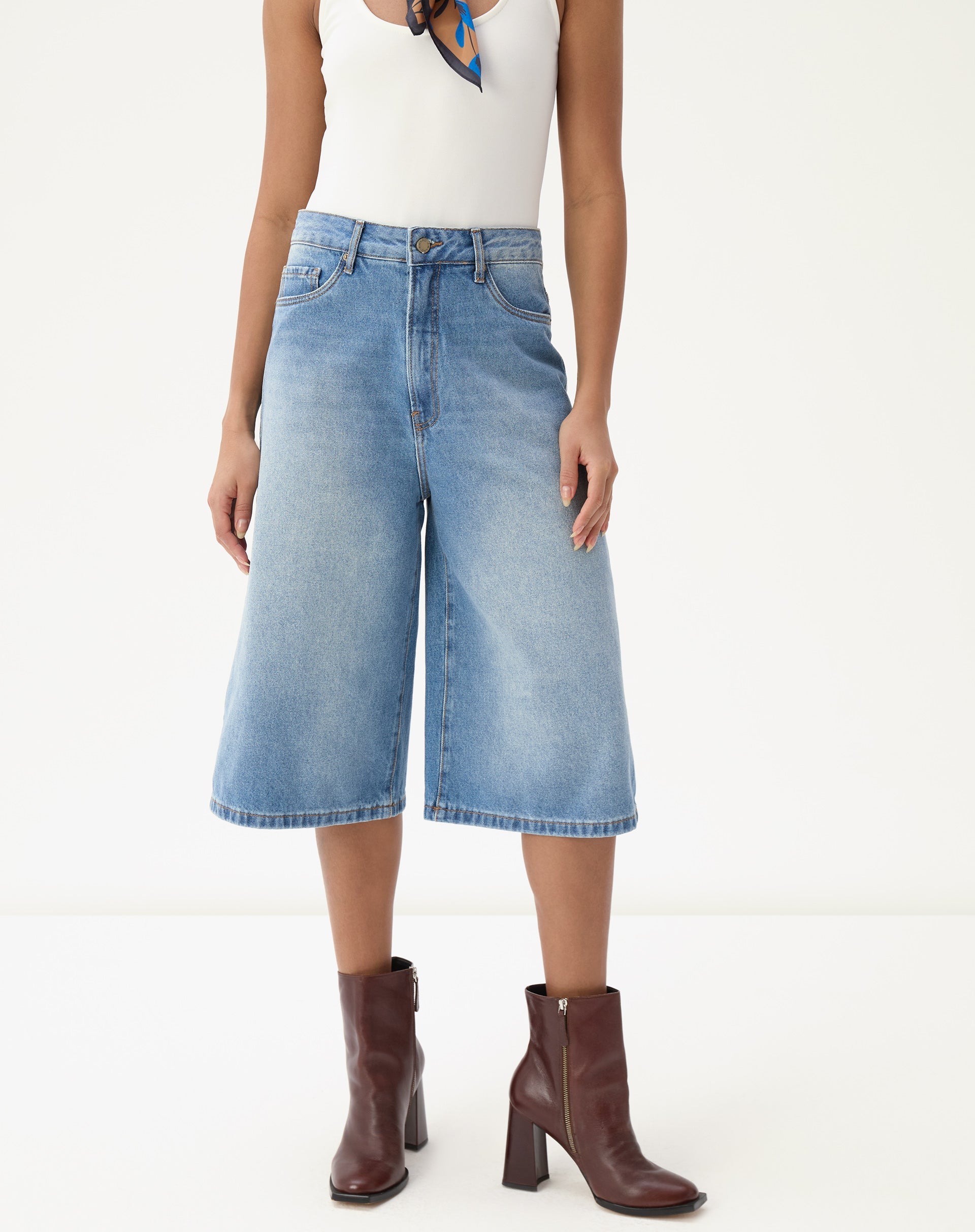 Modelo vestindo bermuda jeans alongada evasê com botas marrons.