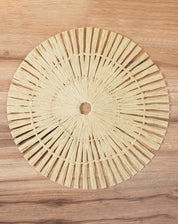 Imagem de um lugar americano redondo feito de papel, com design radial em cor bege, sobre uma superfície de madeira.