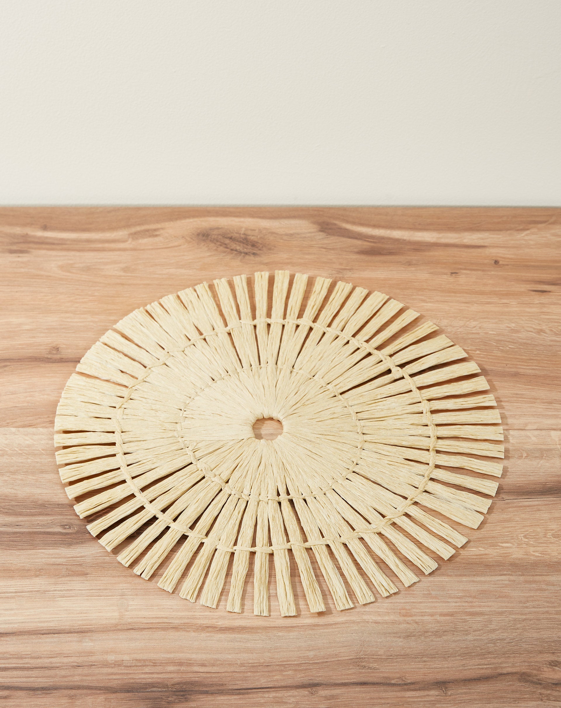 Vista lateral de um lugar americano redondo em papel, mostrando detalhes do padrão radial em cor bege.