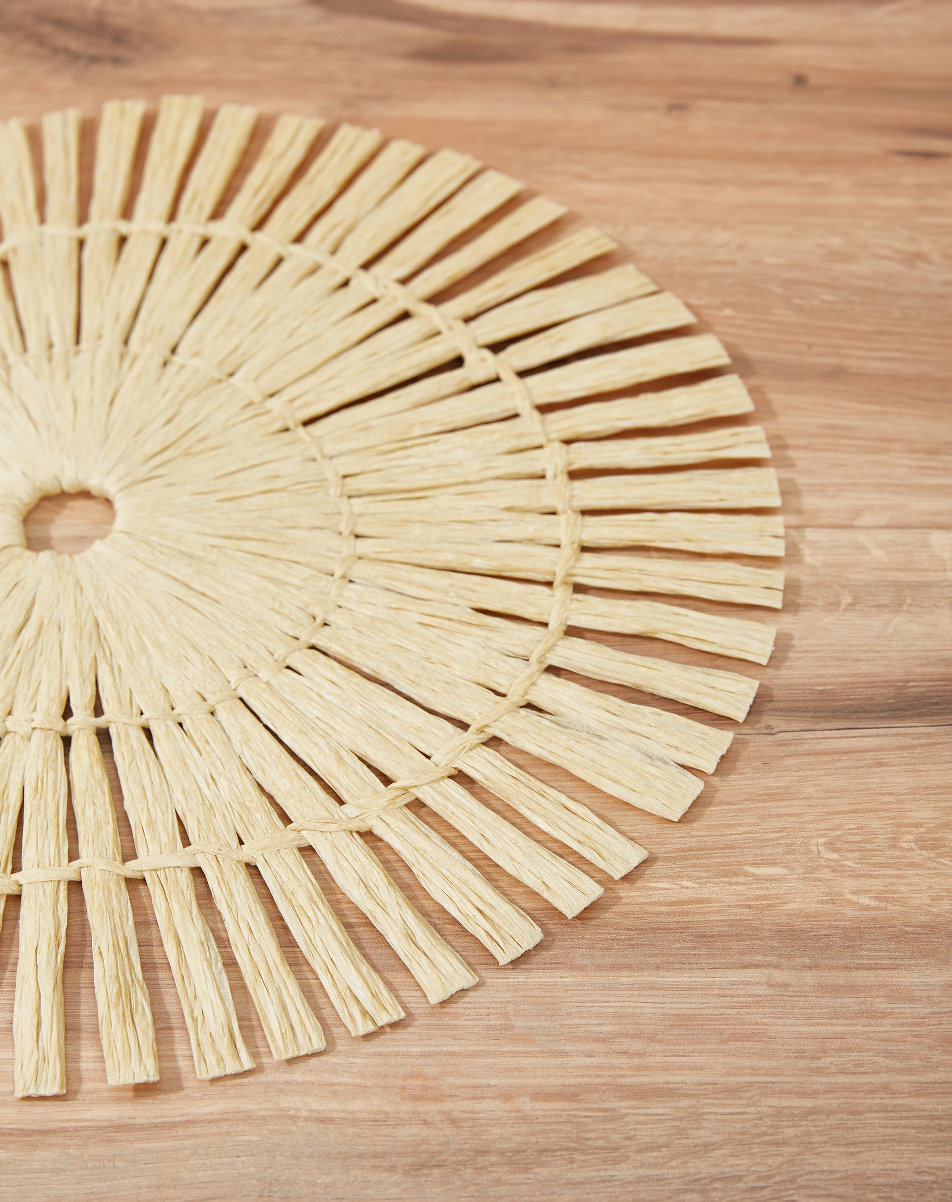 Close-up de um lugar americano redondo em papel, destacando o entrelaçamento das tiras em cor bege.