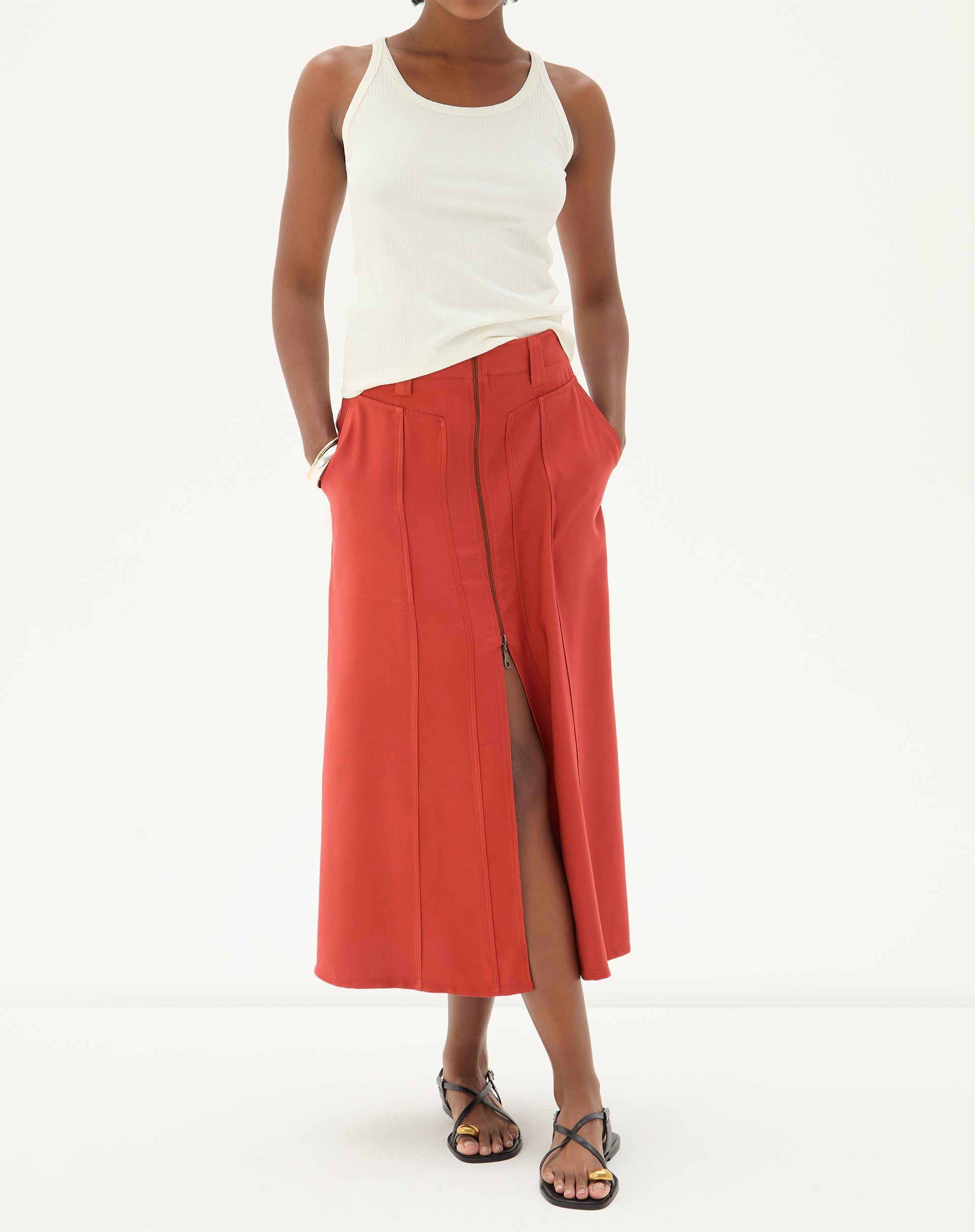 Modelo vestindo regata decote U de malha ribana off-white com saia vermelha e sandálias.