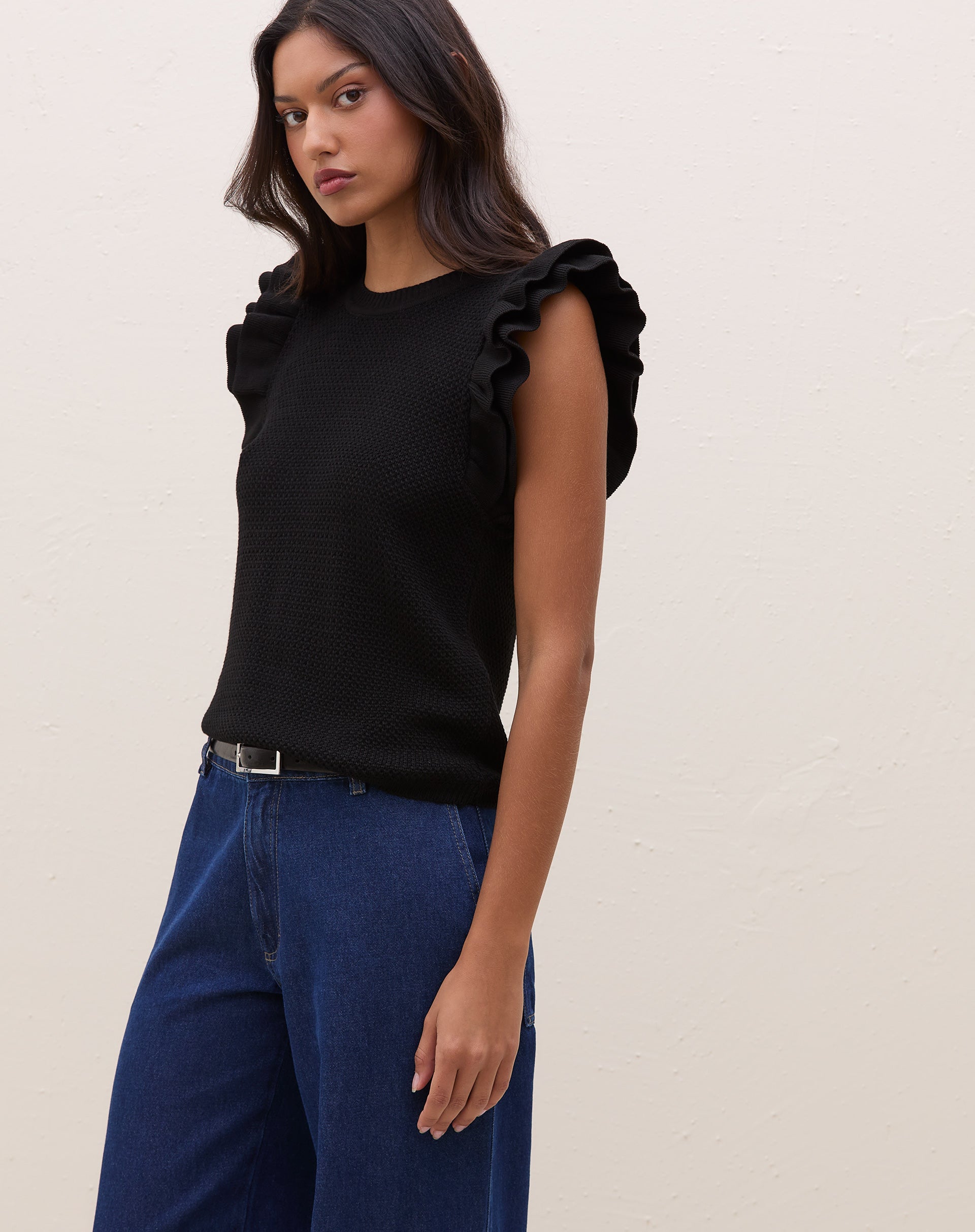 Modelo vestindo blusa de tricot preta com manga de babados, combinada com calça jeans.