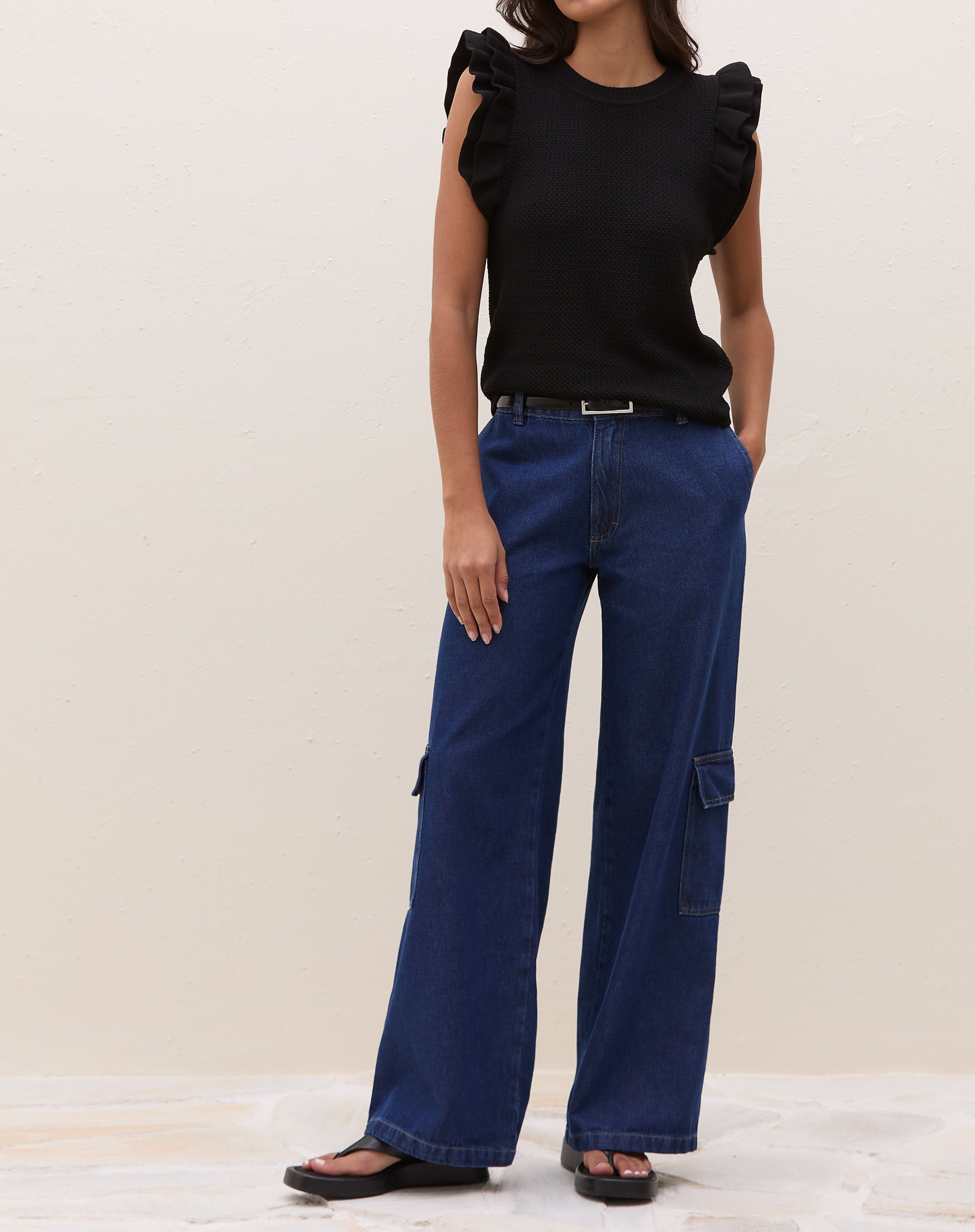 Modelo em pose lateral vestindo blusa de tricot preta com manga de babados.