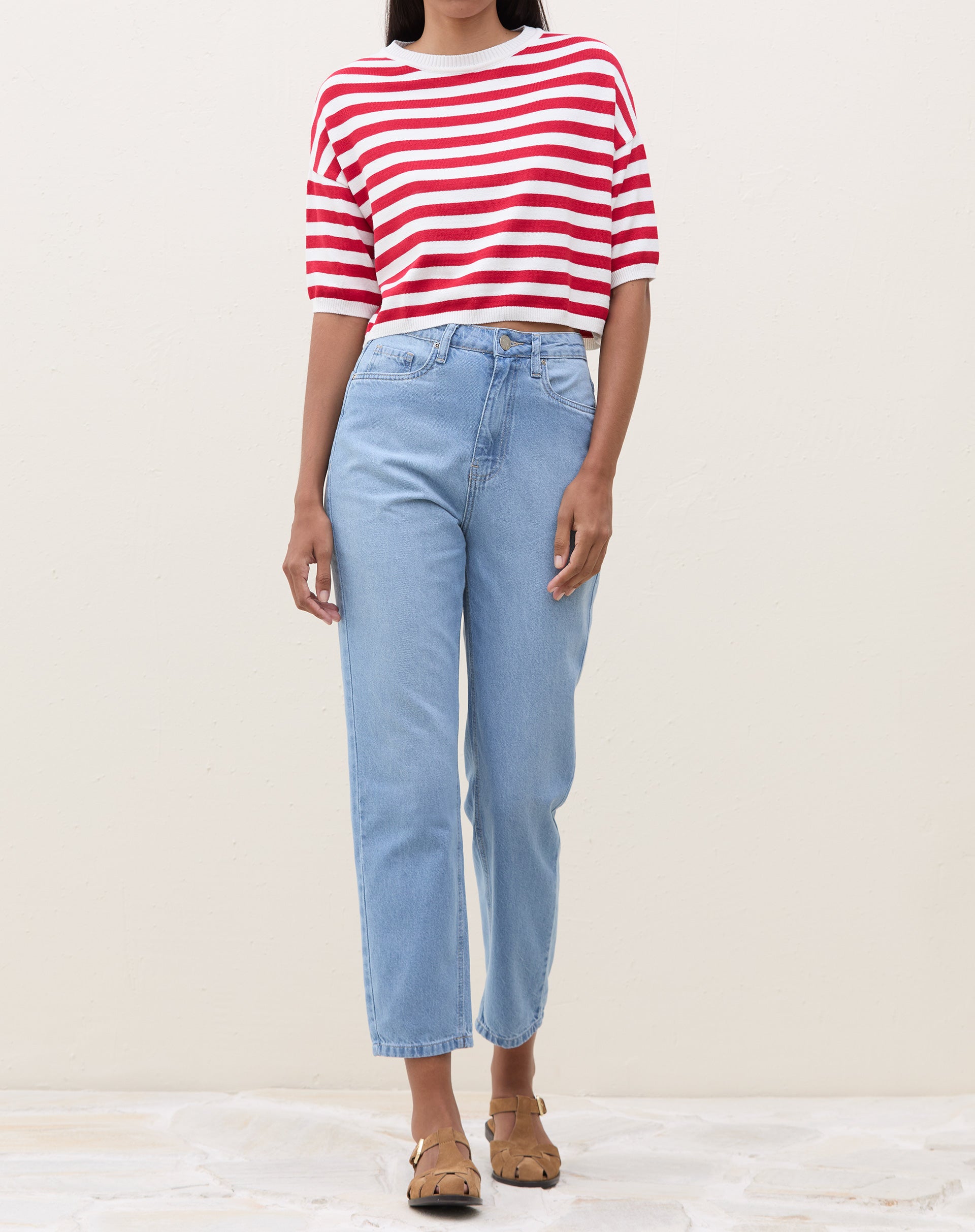 Modelo vestindo camiseta cropped de tricot listrada em vermelho e branco com calça jeans.
