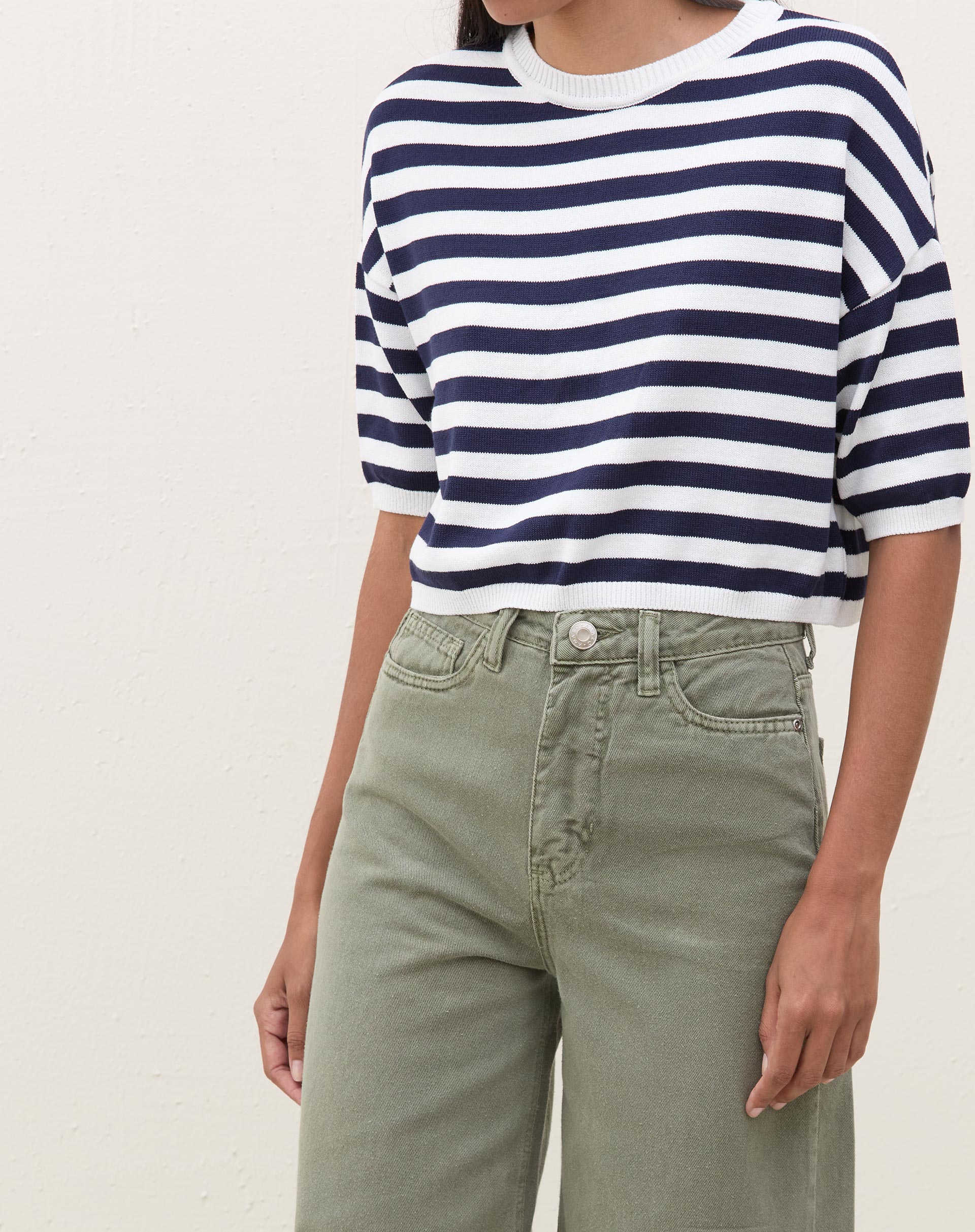 Vista lateral da camiseta cropped de tricot listrada azul marinho e branco.