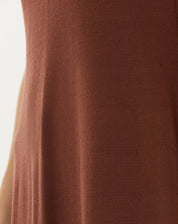 Imagem lateral da modelo vestindo o vestido midi de tricot marrom, com acessórios minimalistas.