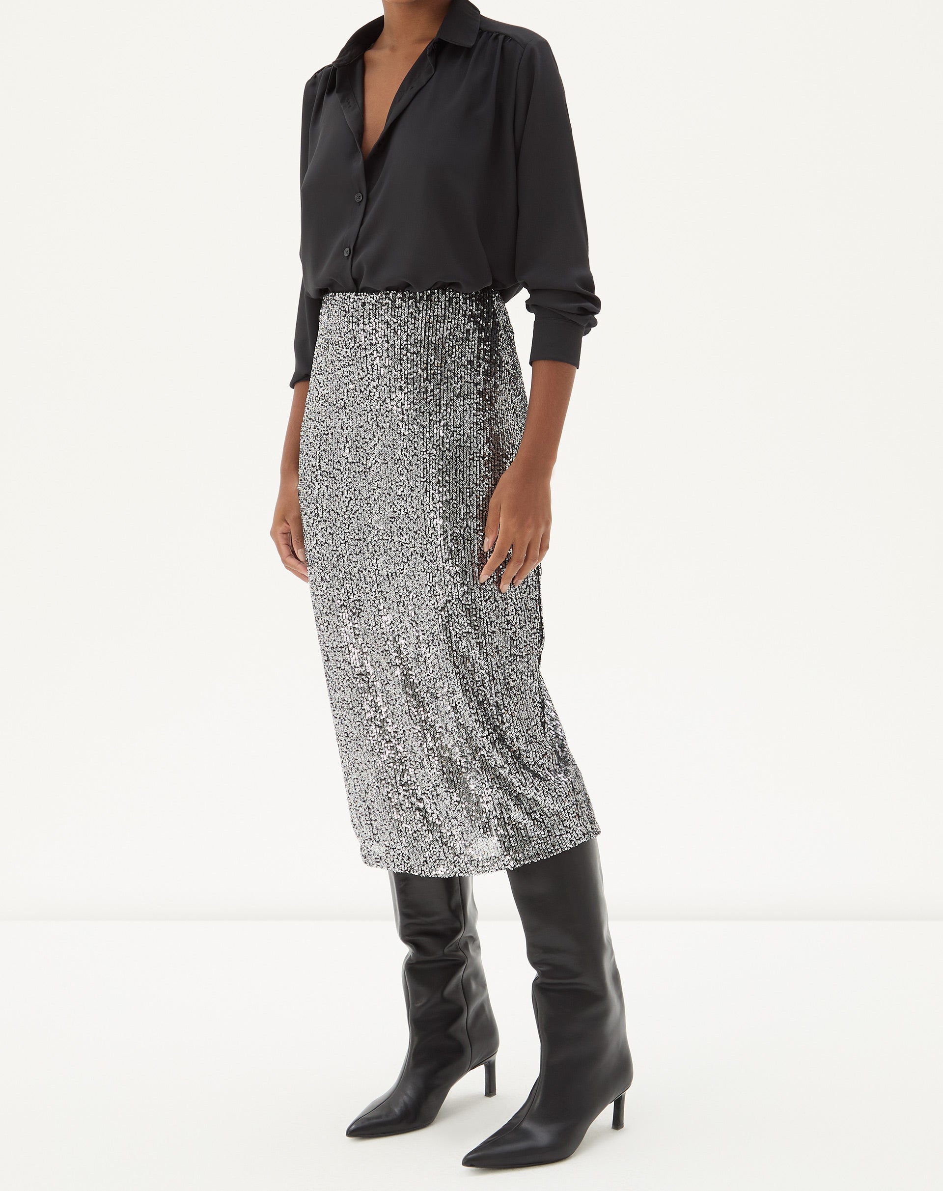 Modelo vestindo a Saia Midi Tubo de Paetê - Prata com camisa preta e botas pretas, vista frontal.