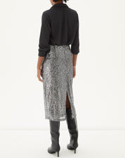 Modelo vestindo a Saia Midi Tubo de Paetê - Prata com camisa preta e botas pretas, vista traseira.