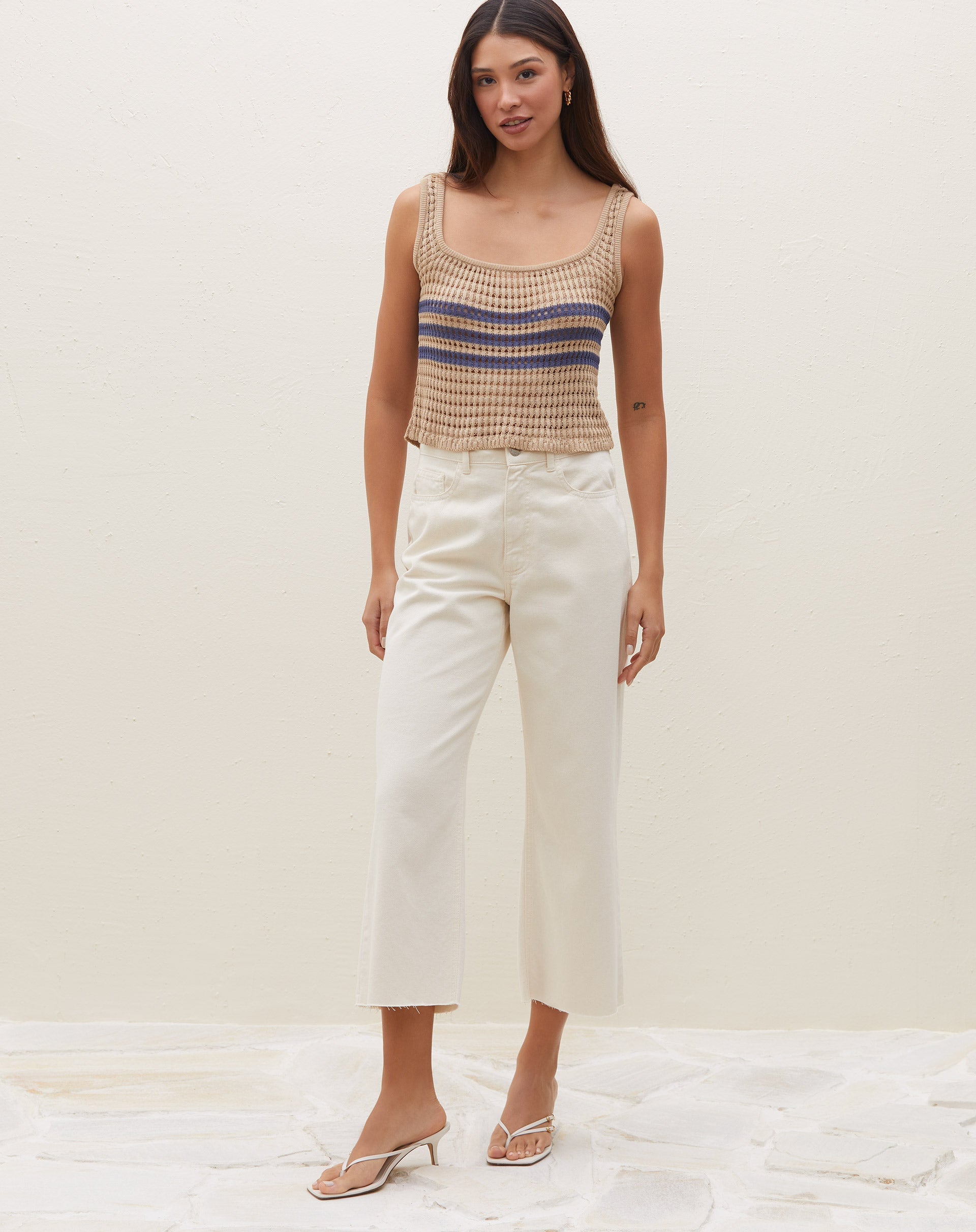 Modelo vestindo calça sarja wide cropped off-white com top de crochê listrado, vista lateral.