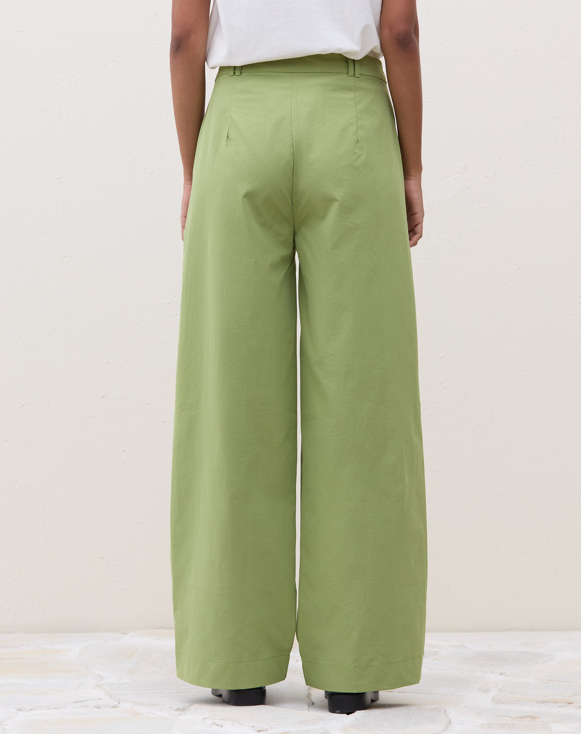 Modelo vestindo calça wide verde com cardigan bege e sapatos marrons.