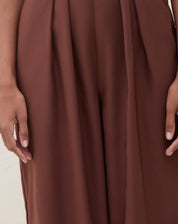 Imagem de um macacão marrom com pregas, mostrando detalhes das pernas.