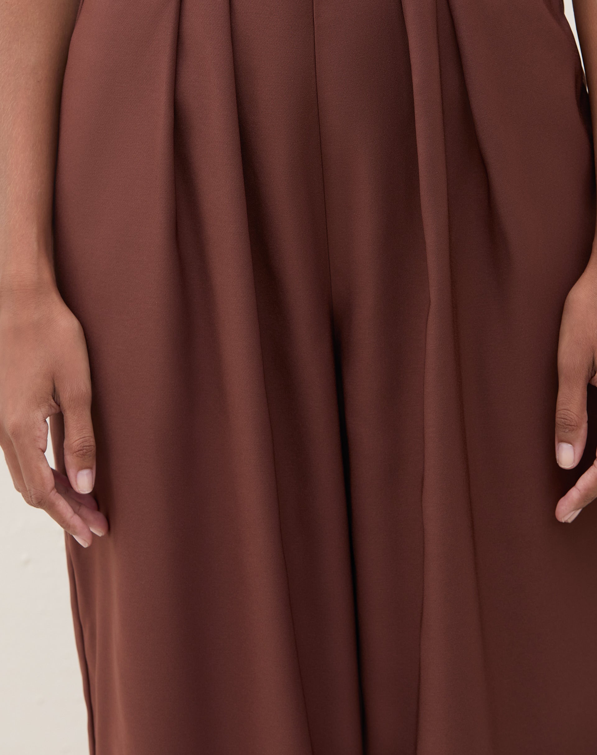 Imagem de um macacão marrom com pregas, mostrando detalhes das pernas.