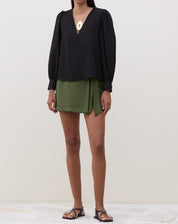 Modelo vestindo blusa preta com manga longa e decote V, combinada com saia verde.