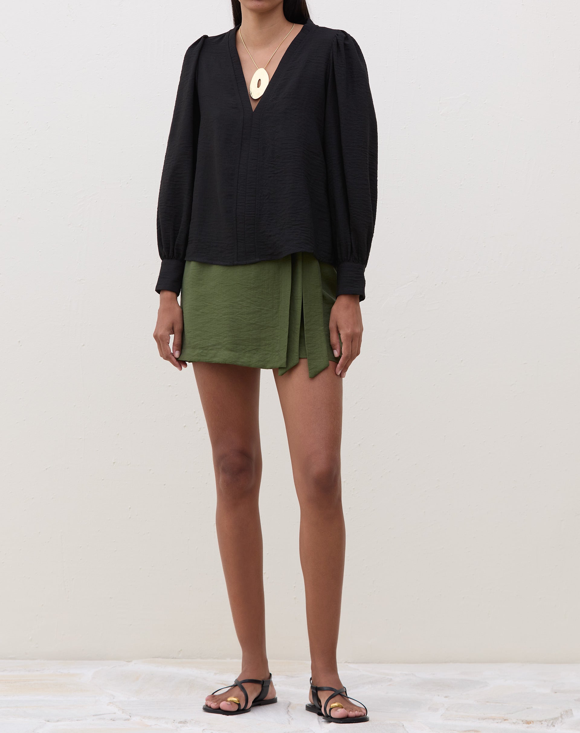 Modelo vestindo blusa preta com manga longa e decote V, combinada com saia verde.