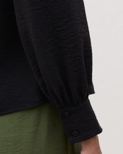 Detalhe da manga longa com punho abotoado da blusa preta.