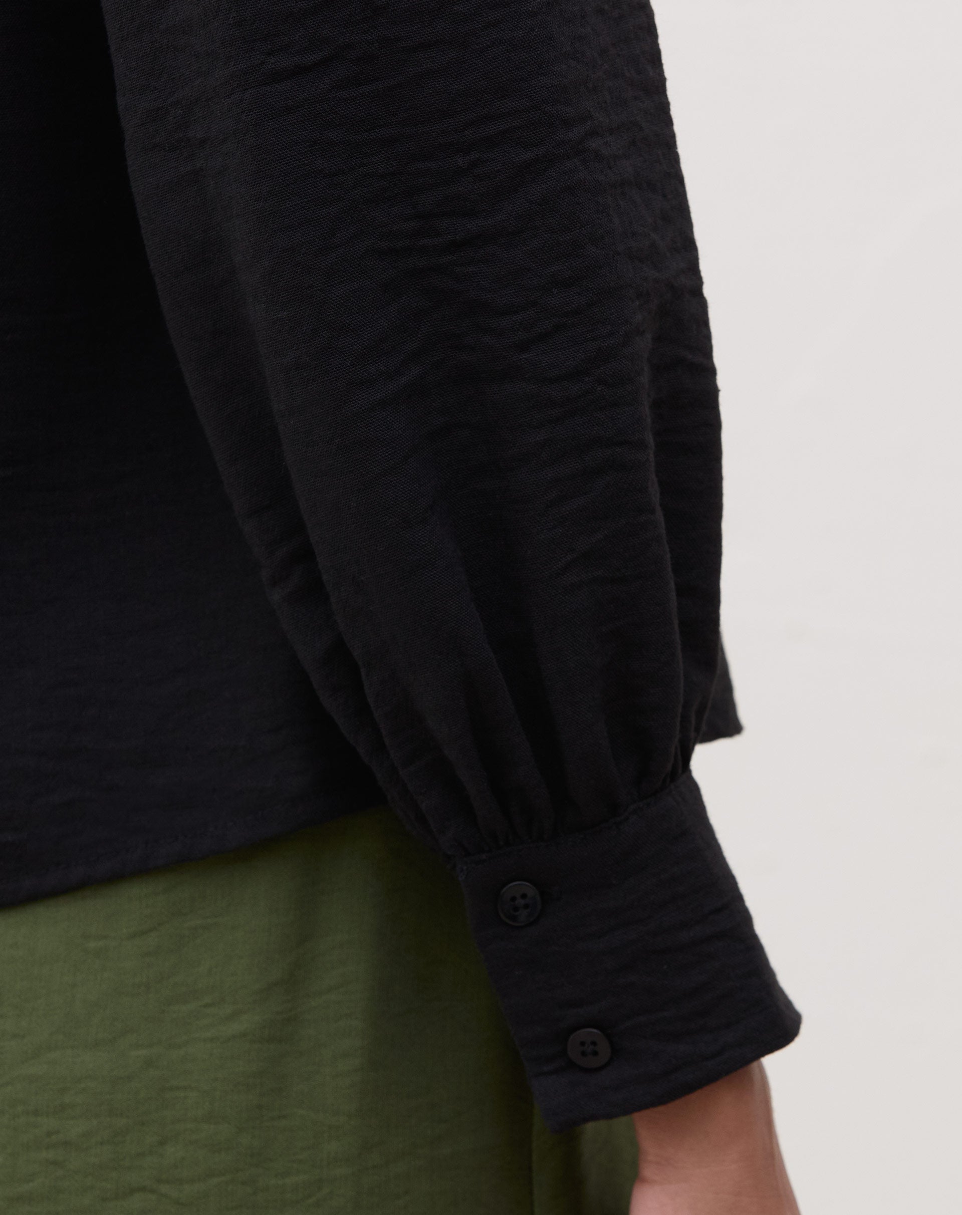Detalhe da manga longa com punho abotoado da blusa preta.