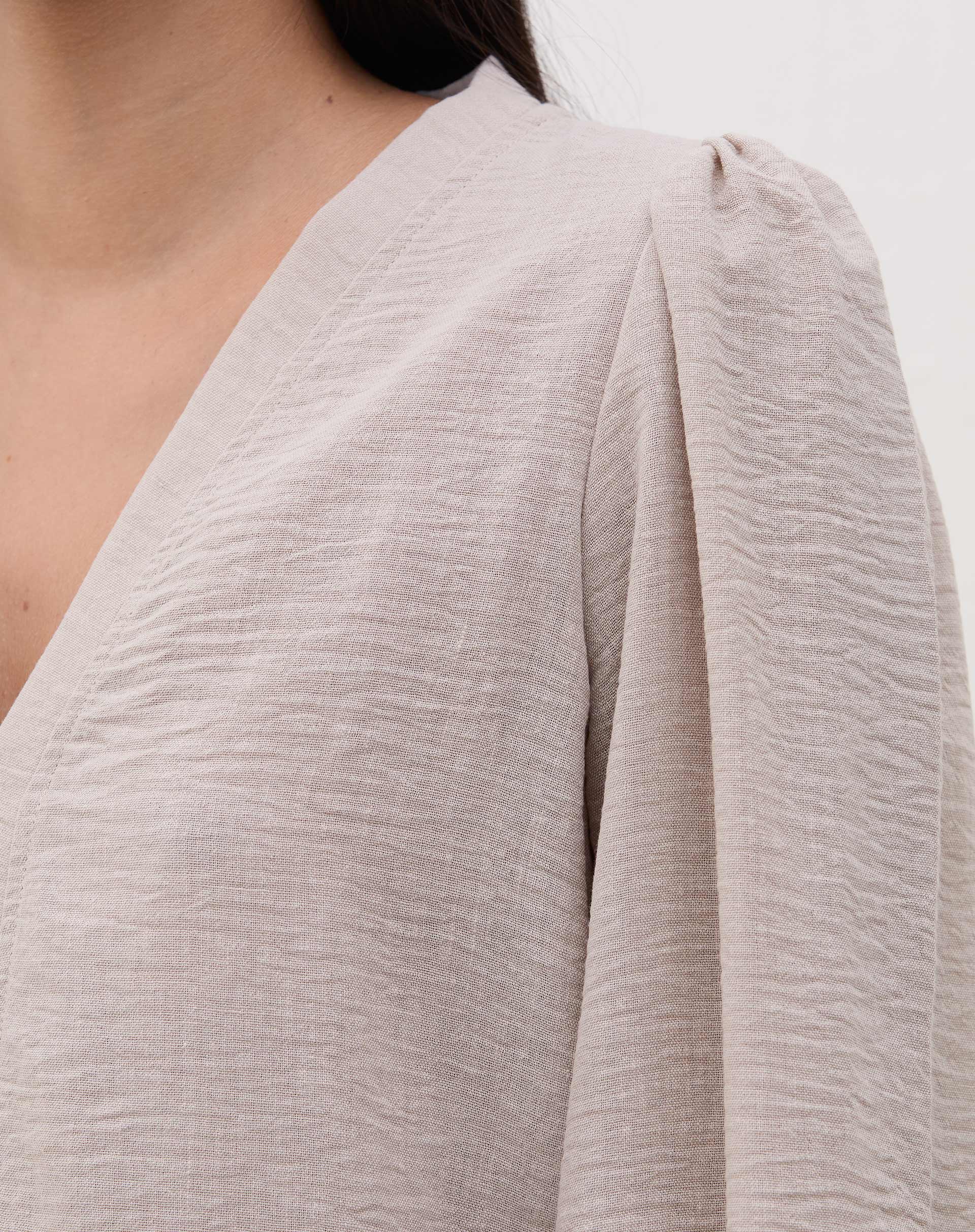 Detalhe do decote V da blusa bege.