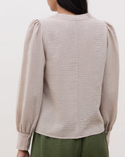 Vista lateral da blusa bege mostrando o caimento.