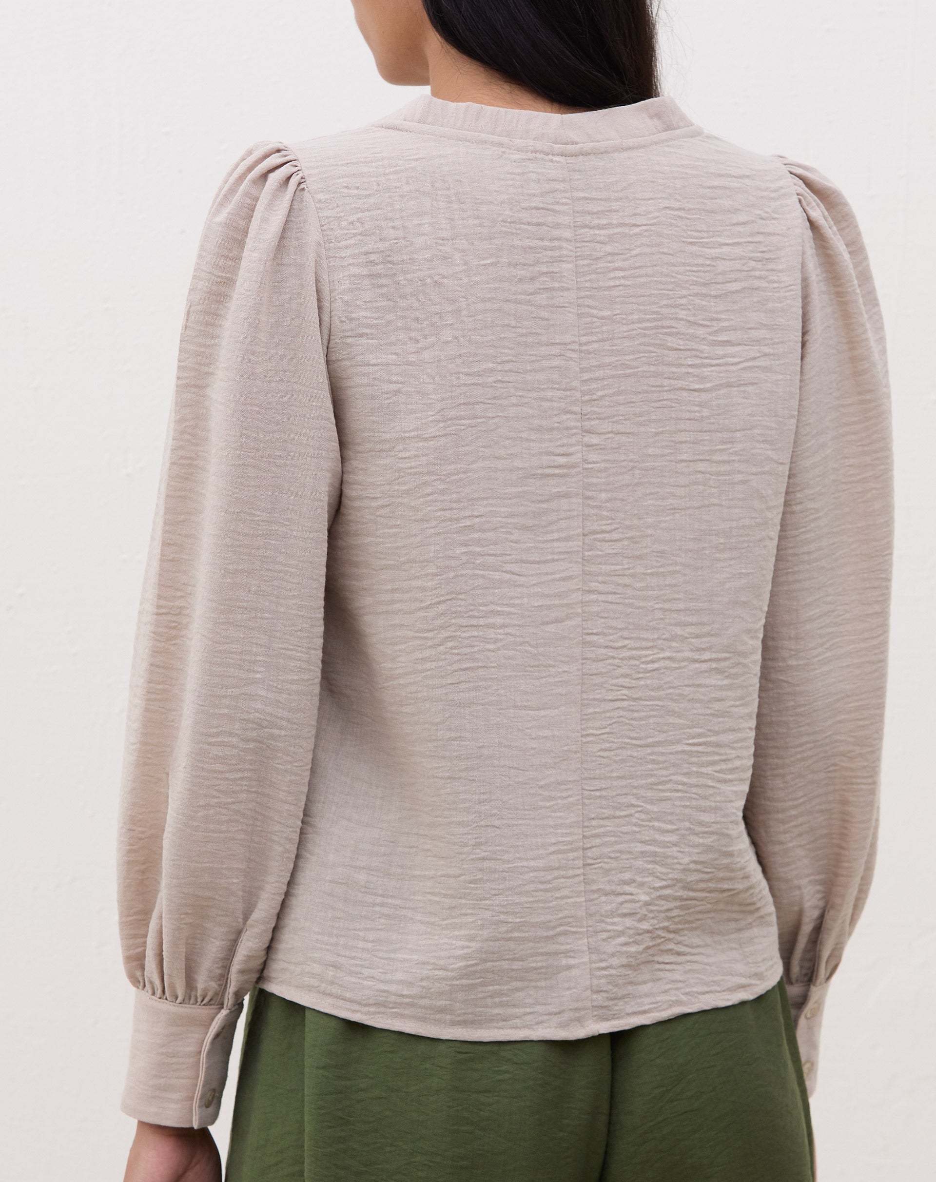 Vista lateral da blusa bege mostrando o caimento.