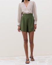 Modelo vestindo a blusa bege com shorts verdes.