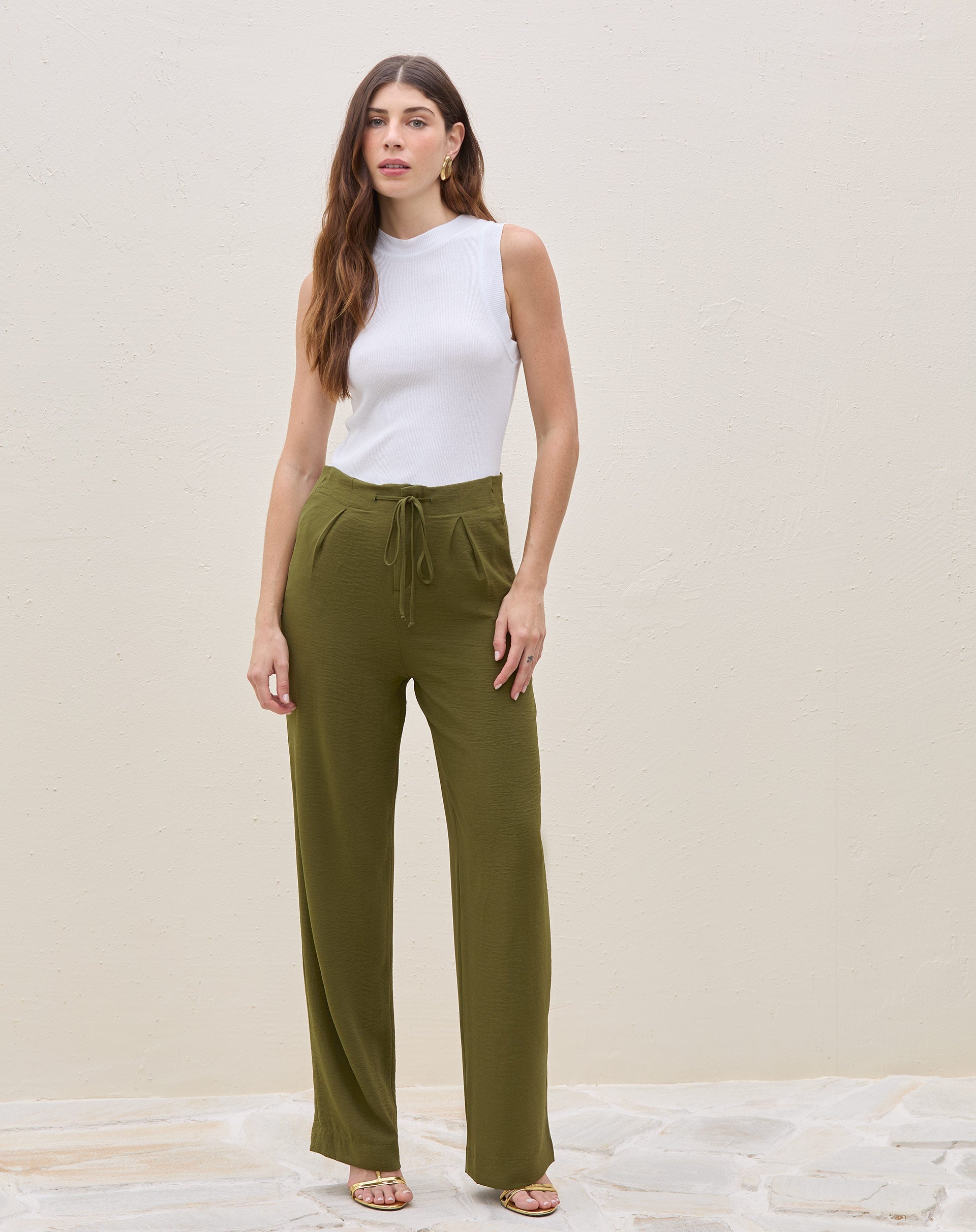 Modelo vestindo calça reta verde militar com blusa branca sem mangas, vista frontal.